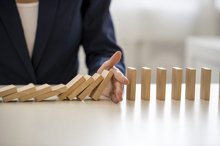 Wooden dominoes on a table falling with a hand stopping them